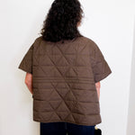 Person wearing a brown quilted jacket against a white background