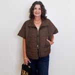 Woman wearing a brown vest and holding a black handbag with gold accents against a white background