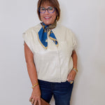 Woman wearing a white blouse with a blue scarf and jeans against a white background