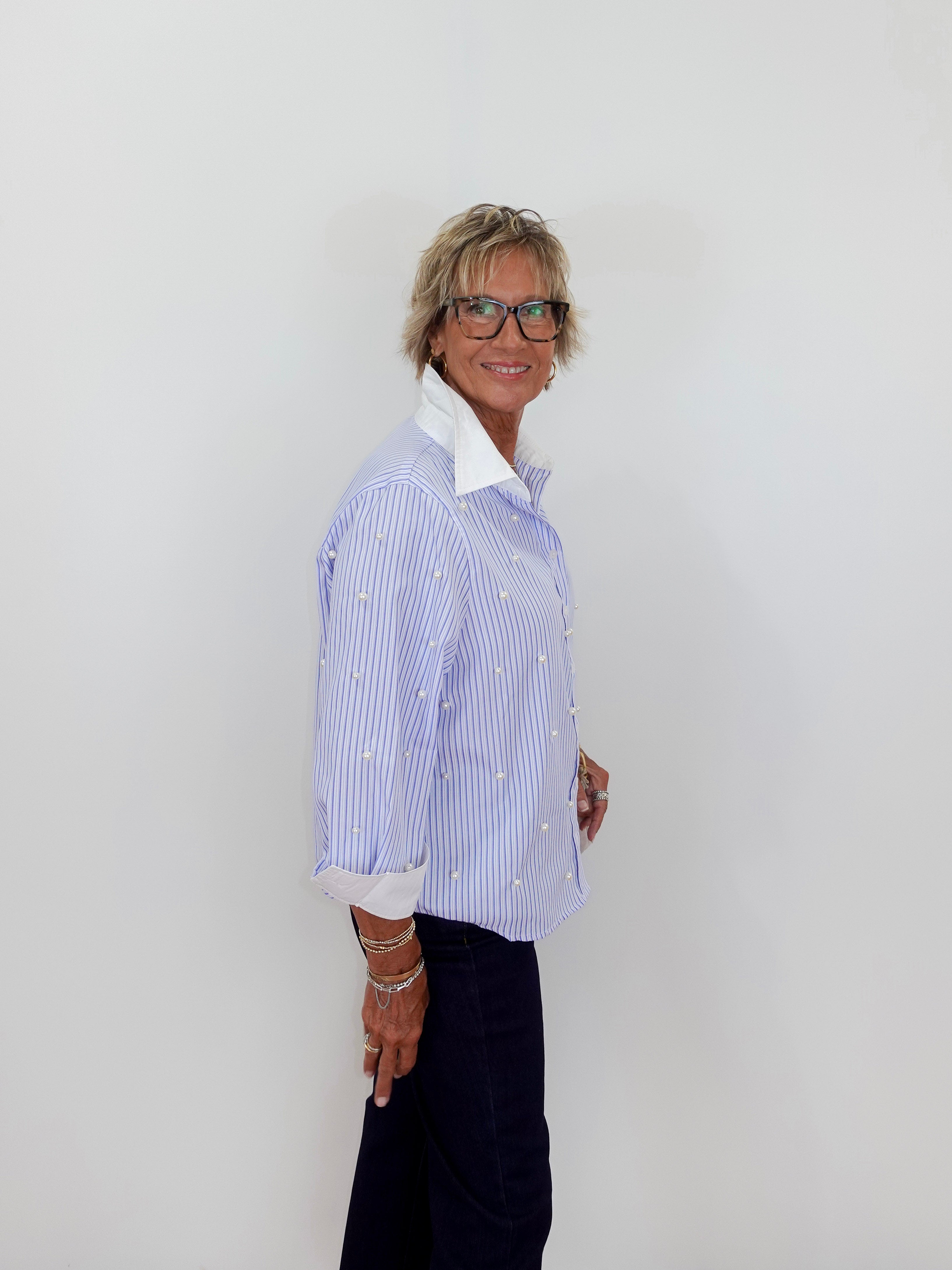 Person wearing a blue and white striped shirt with a white collar against a plain background