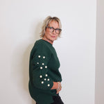 Person wearing a green sweater with button details against a white wall