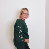 Person wearing a green sweater with button details against a white wall