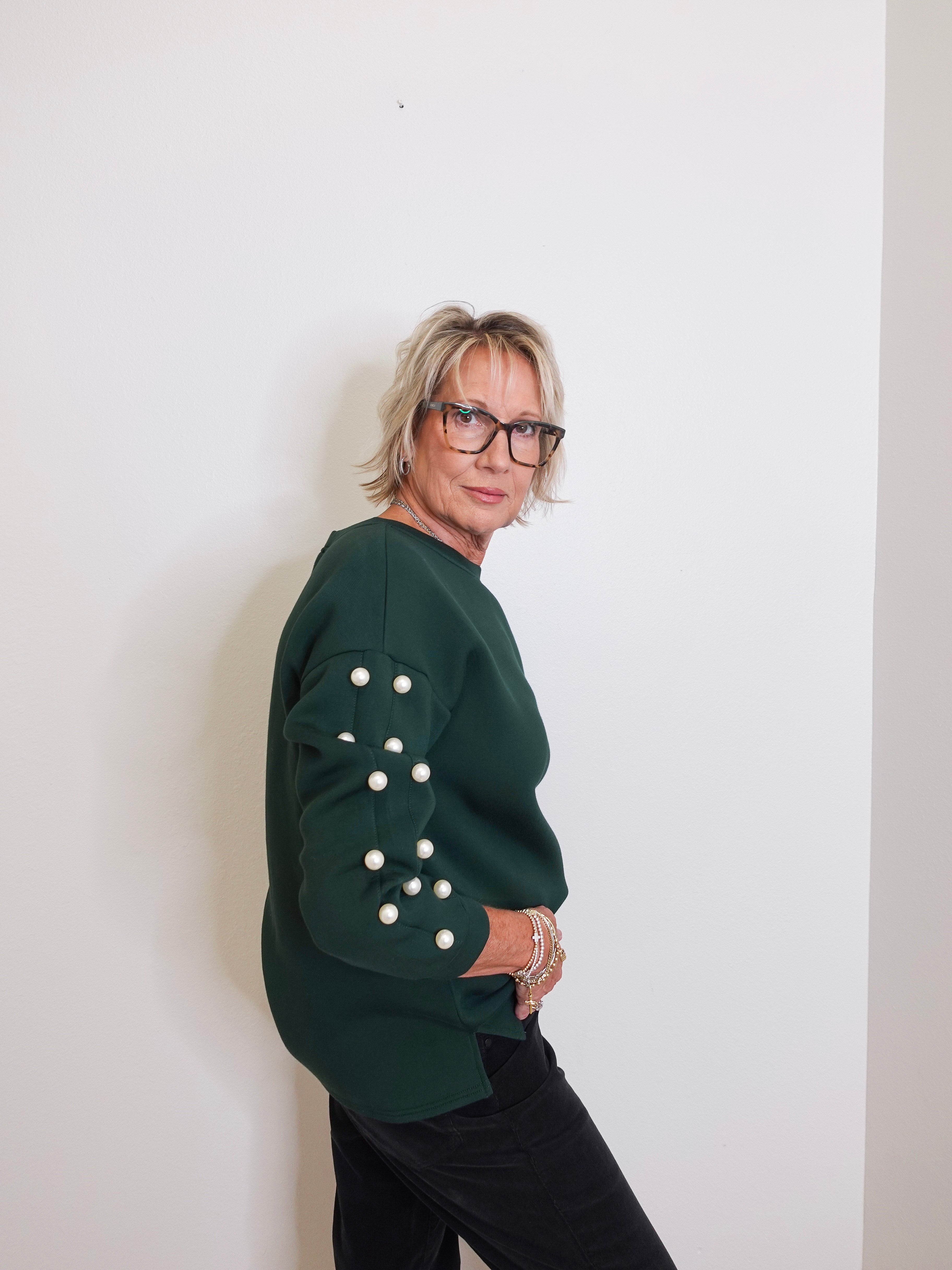 Person wearing a green sweater with button details against a white wall