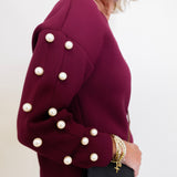 Woman wearing a burgundy dress with pearl buttons, holding a black handbag.