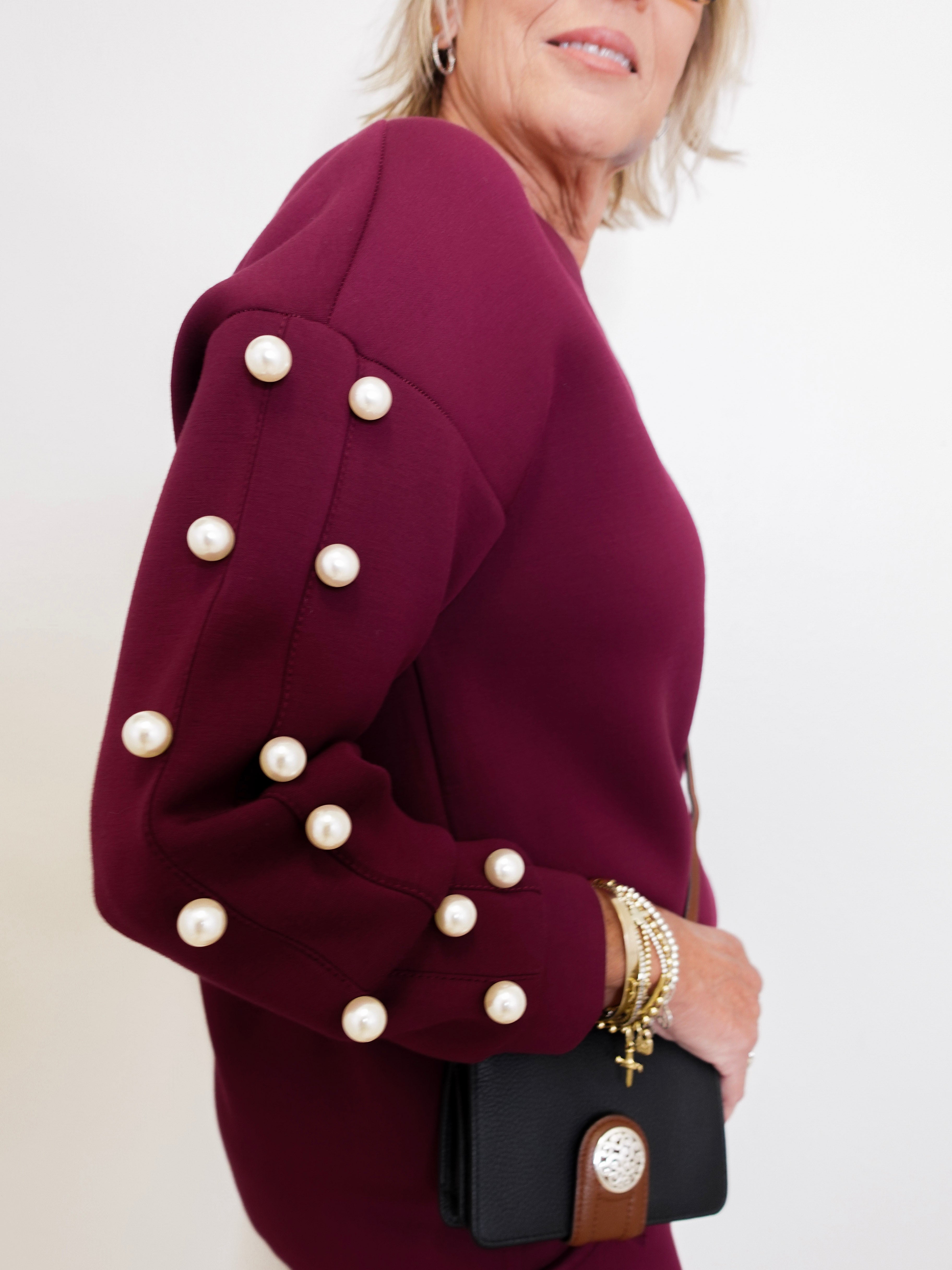 Woman wearing a burgundy dress with pearl buttons, holding a black handbag.