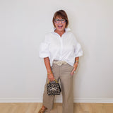 Woman wearing a white shirt, beige pants, and brown shoes against a white wall.