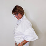 Woman wearing a white blouse with puffed sleeves against a plain background