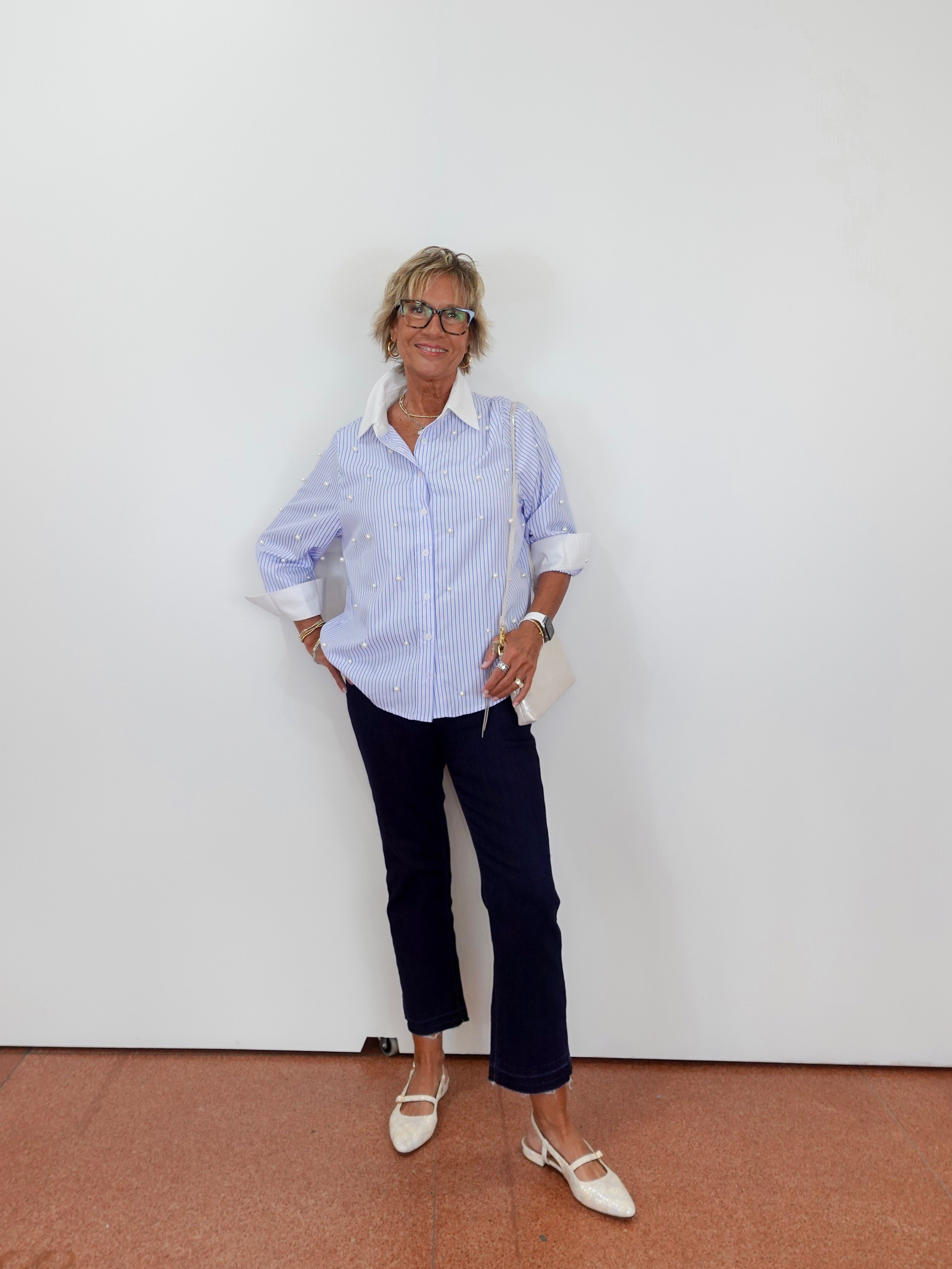 Person wearing a cream outfit with white pants and gray sneakers on a plain background