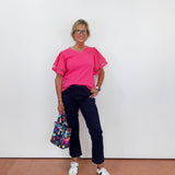 Person wearing a pink top and dark pants, holding a colorful bag against a white wall.