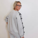 Person wearing a gray outfit with black buttons against a white wall