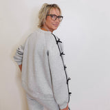 Person wearing a gray outfit with black buttons against a white wall