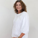 Woman wearing a white blouse and blue jeans against a plain background