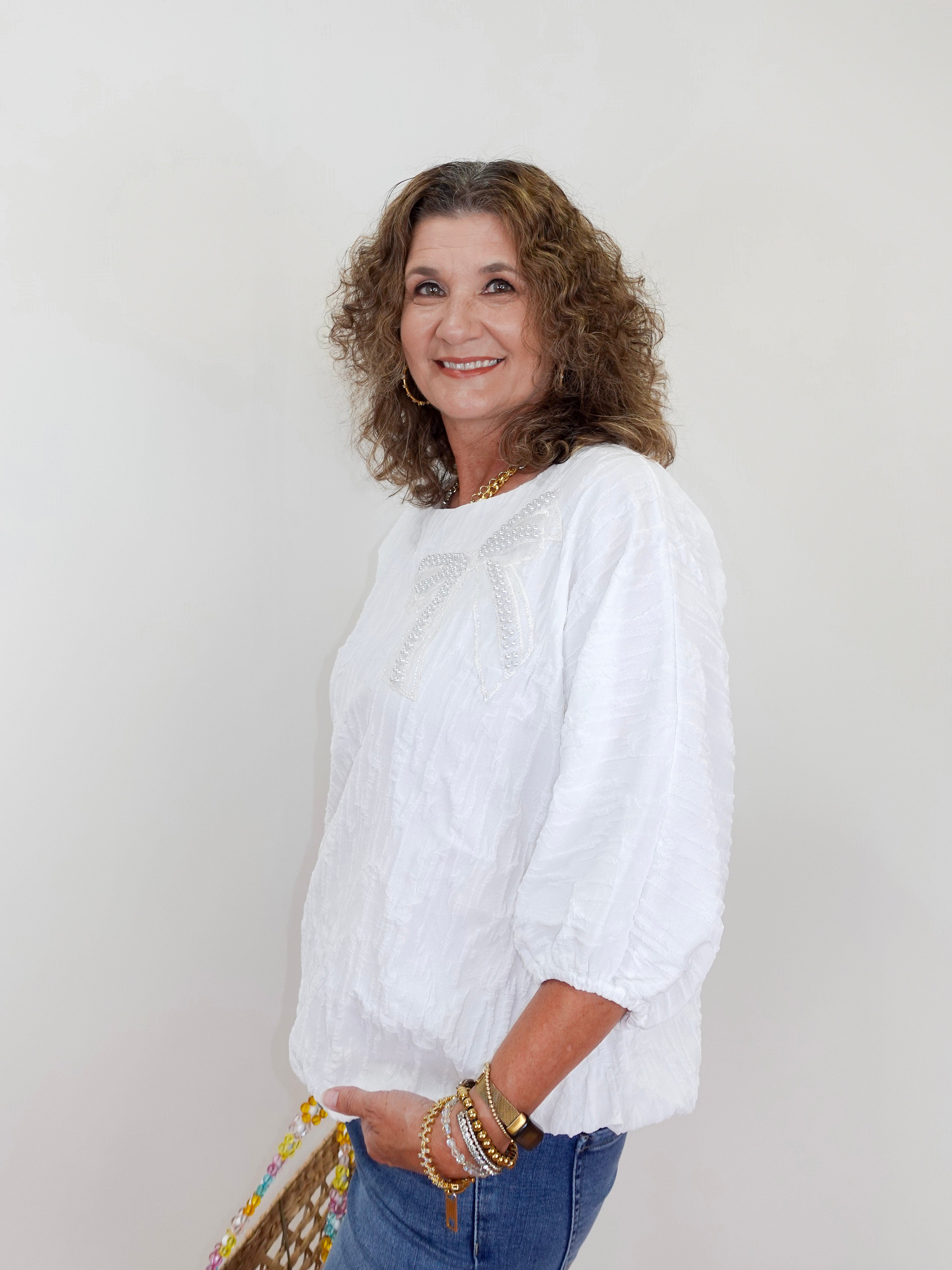 Woman wearing a white blouse and blue jeans against a plain background