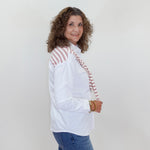 Woman wearing a white blouse with red accents and blue jeans against a plain background