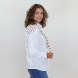 Woman wearing a white blouse with red accents and blue jeans against a plain background