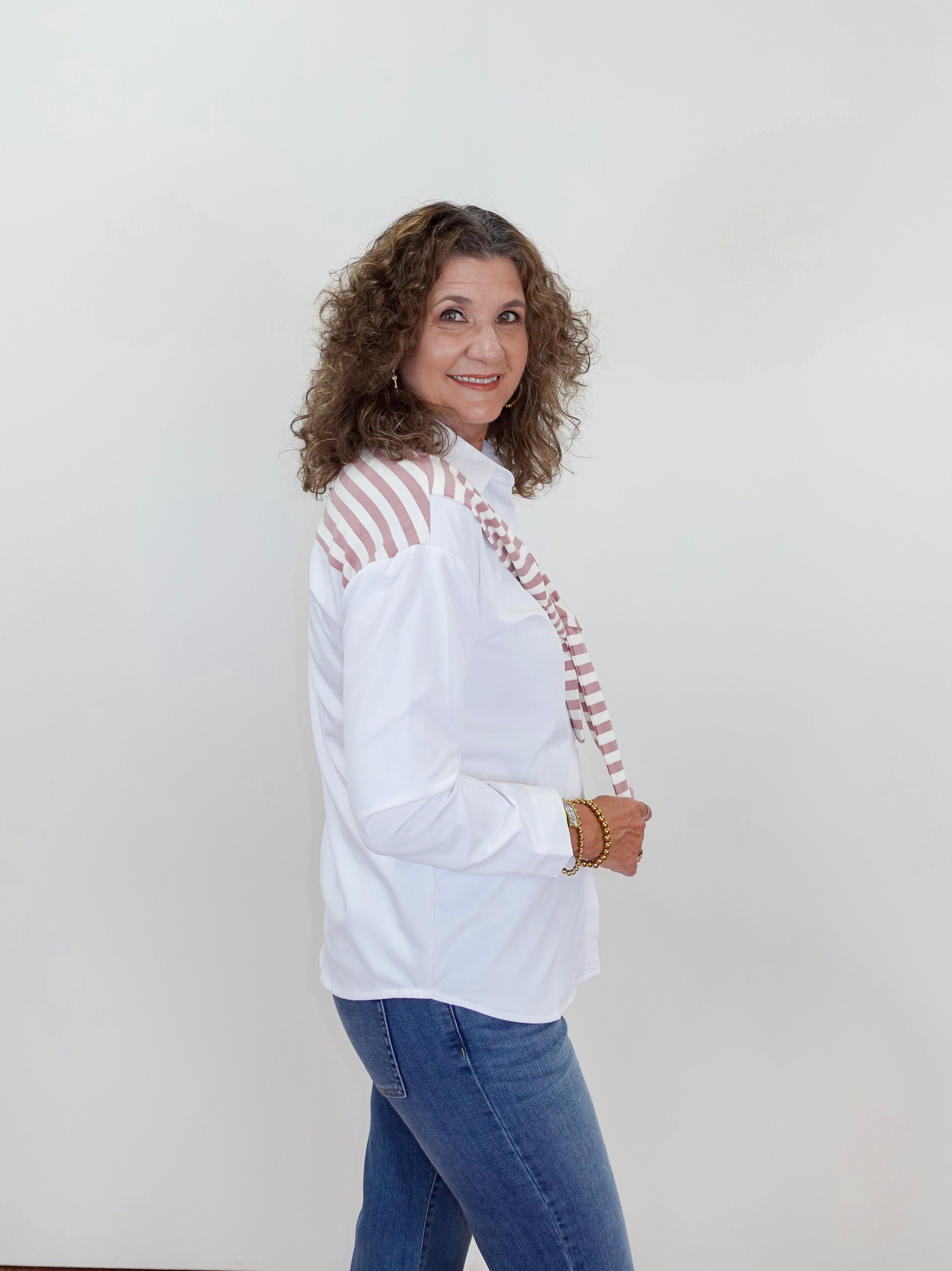 Woman wearing a white blouse with red accents and blue jeans against a plain background