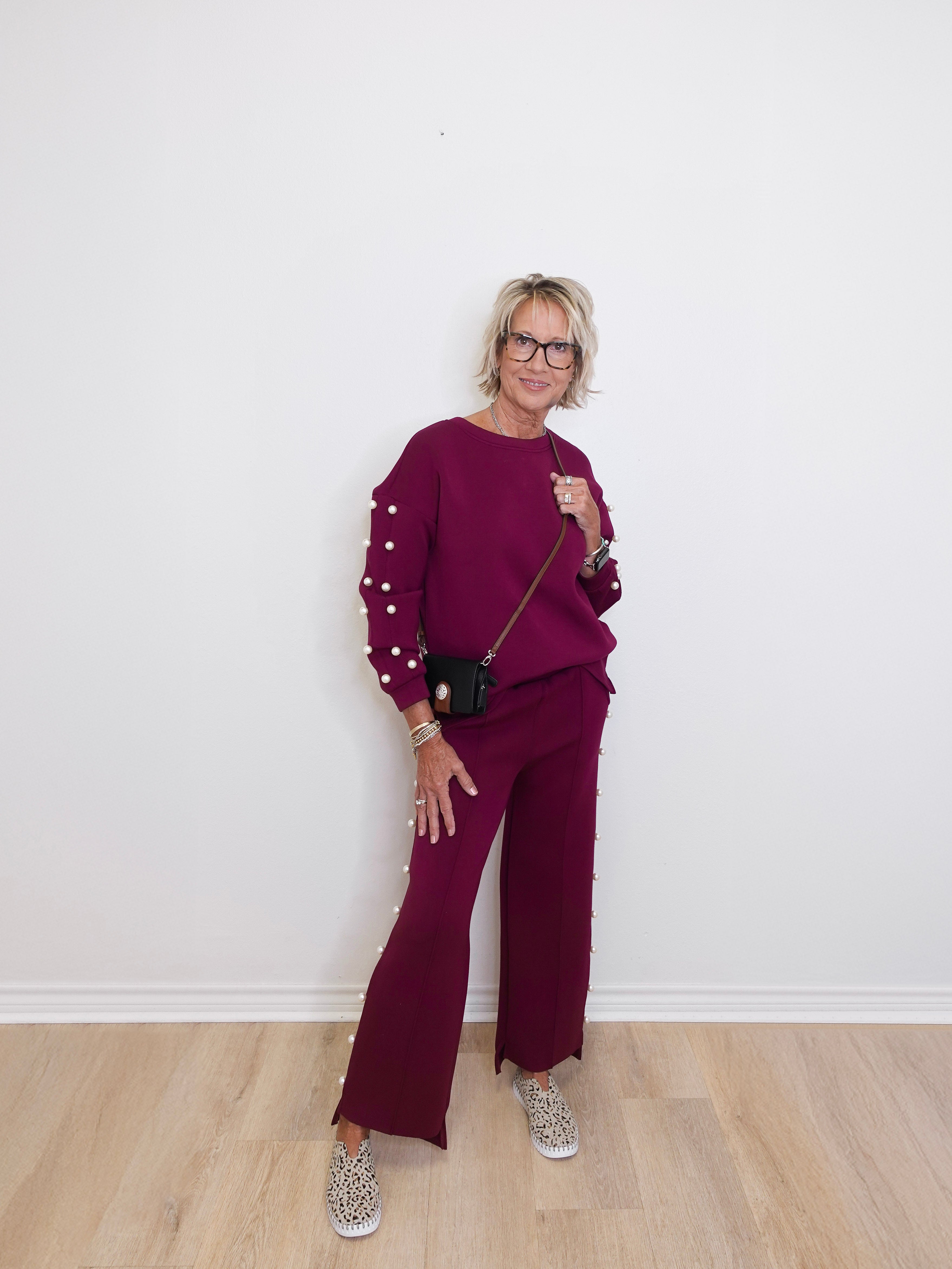 Woman wearing a maroon outfit with pearl details against a white wall.