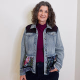 Woman wearing a denim jacket with floral patches against a plain background