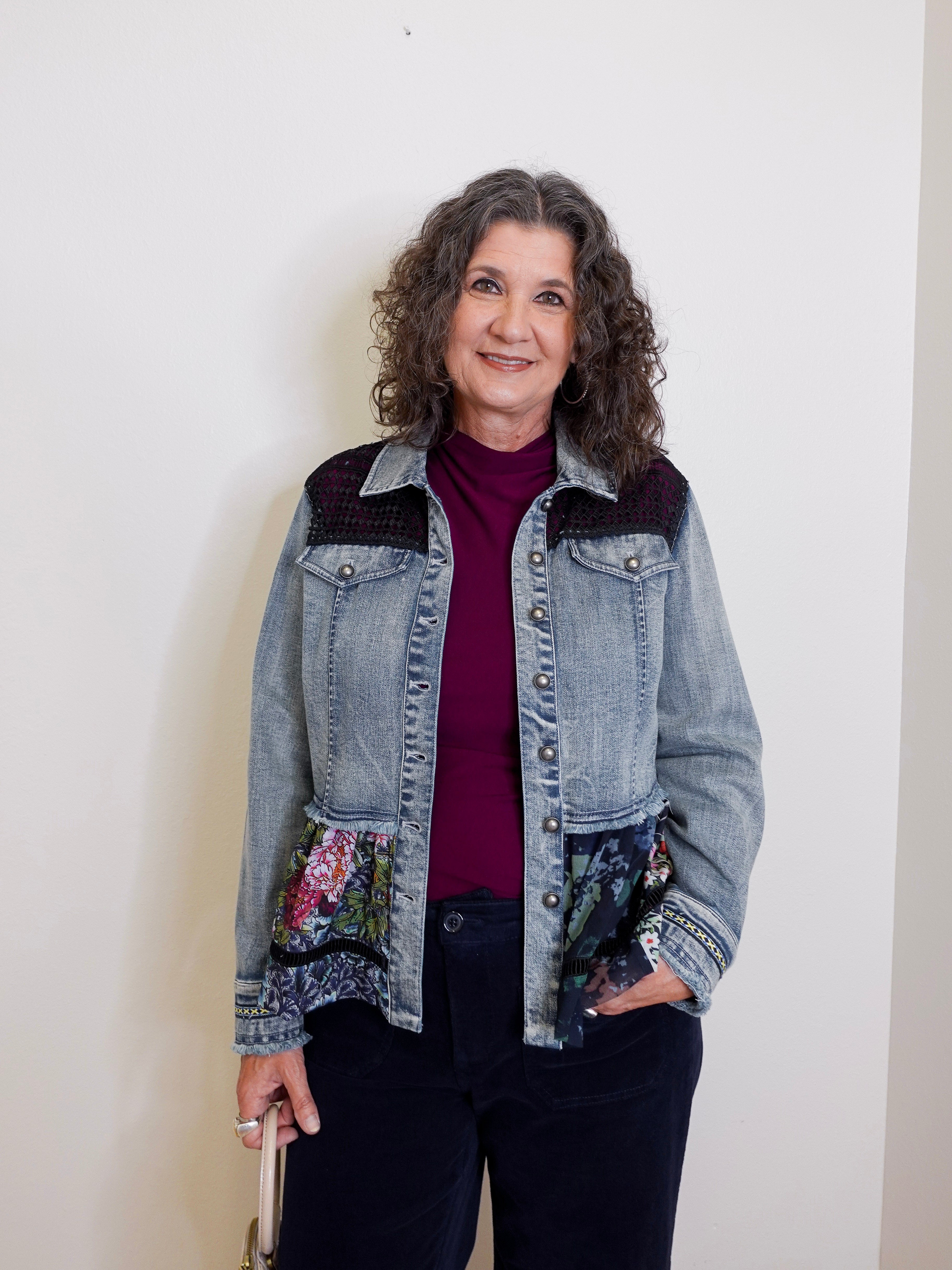 Woman wearing a denim jacket with floral patches against a plain background