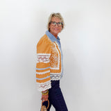 Woman wearing a mustard yellow jacket with lace details against a white wall.