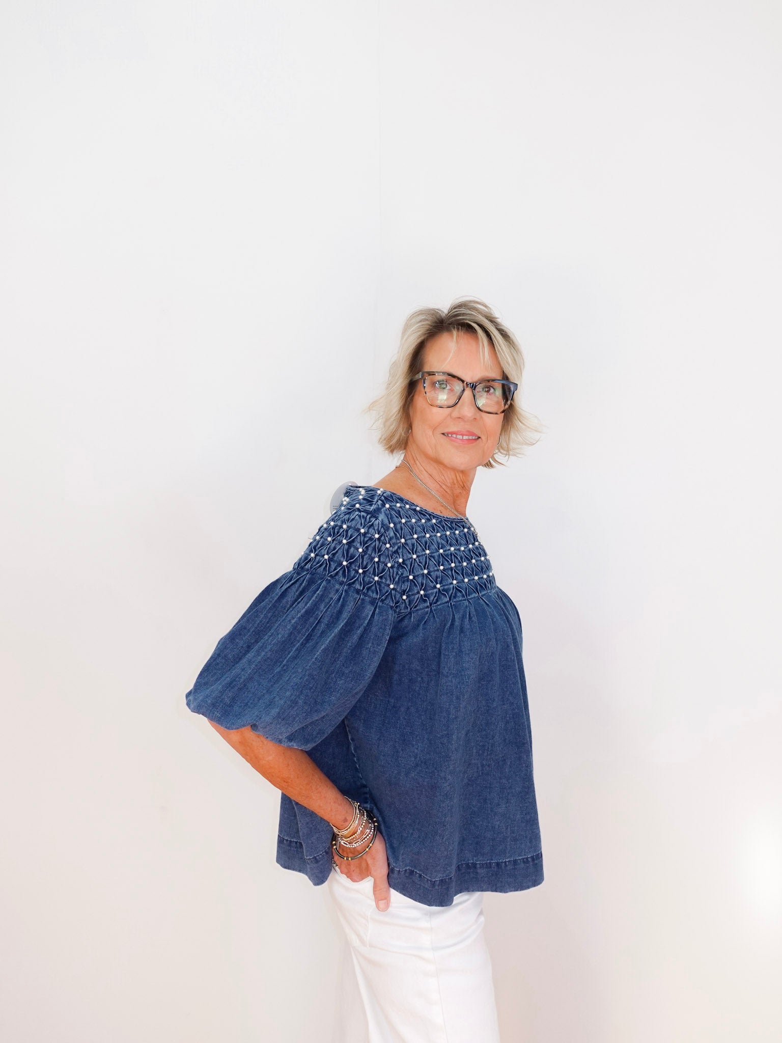 Woman wearing a blue denim top with bead embellishments on a white background