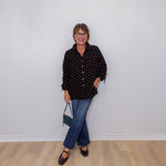 Person wearing a black polka dot shirt and blue jeans against a white wall.