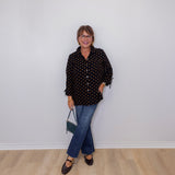 Person wearing a black polka dot shirt and blue jeans against a white wall.