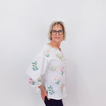 Woman wearing a white blouse with floral embroidery against a plain background