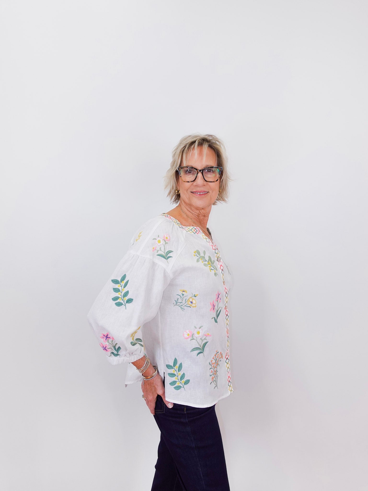 Woman wearing a white blouse with floral embroidery against a plain background