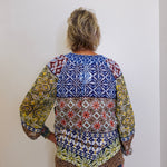 Person wearing a colorful patterned blouse against a white wall