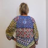 Person wearing a colorful patterned blouse against a white wall