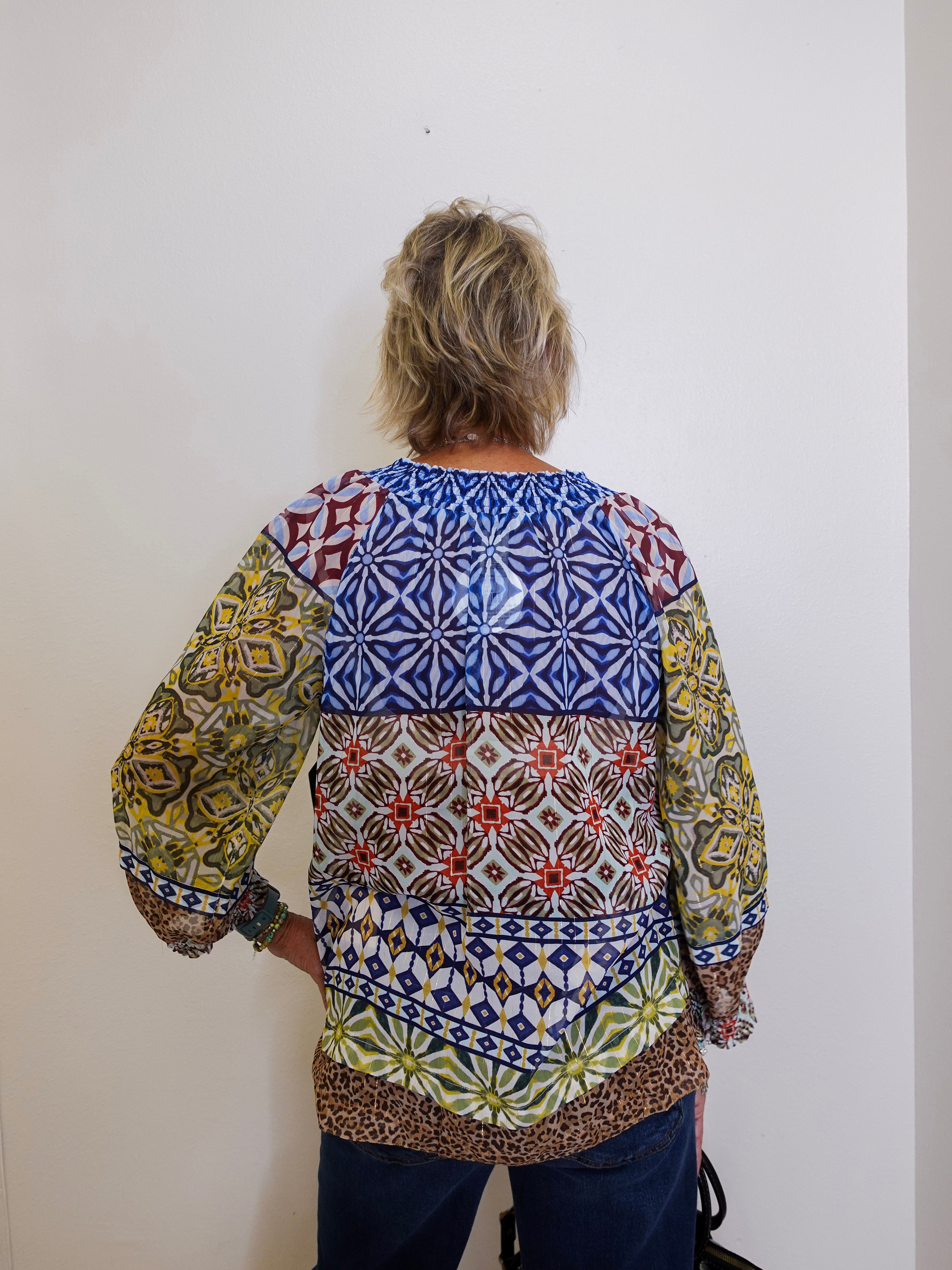 Person wearing a colorful patterned blouse against a white wall