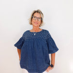 Woman wearing a blue blouse with white polka dots on a plain background