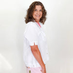 Woman wearing a white shirt and floral pants against a plain background