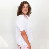 Woman wearing a white shirt and floral pants against a plain background