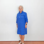 Woman wearing a blue dress standing against a white wall.