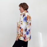 Woman wearing a colorful floral blouse and black shorts against a white wall.