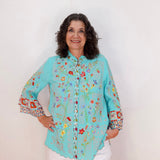 Woman wearing a light blue floral embroidered blouse against a white background