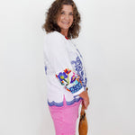 Woman wearing a white embroidered jacket with colorful designs on a plain background