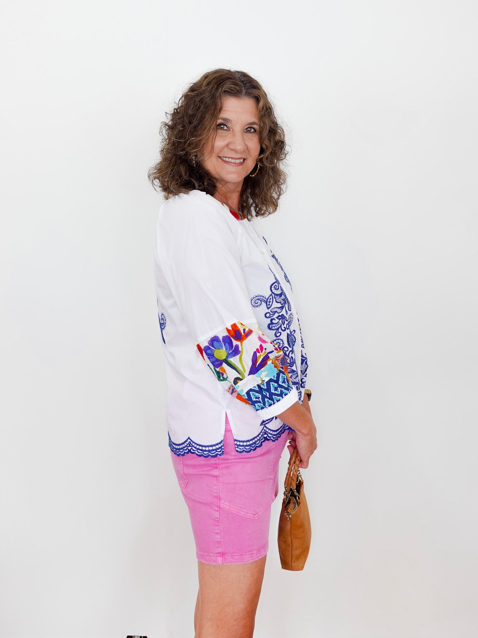Woman wearing a white embroidered jacket with colorful designs on a plain background