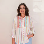 Woman wearing a colorful striped shirt with a geometric pattern on a plain background