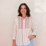 Woman wearing a colorful striped shirt with a geometric pattern on a plain background