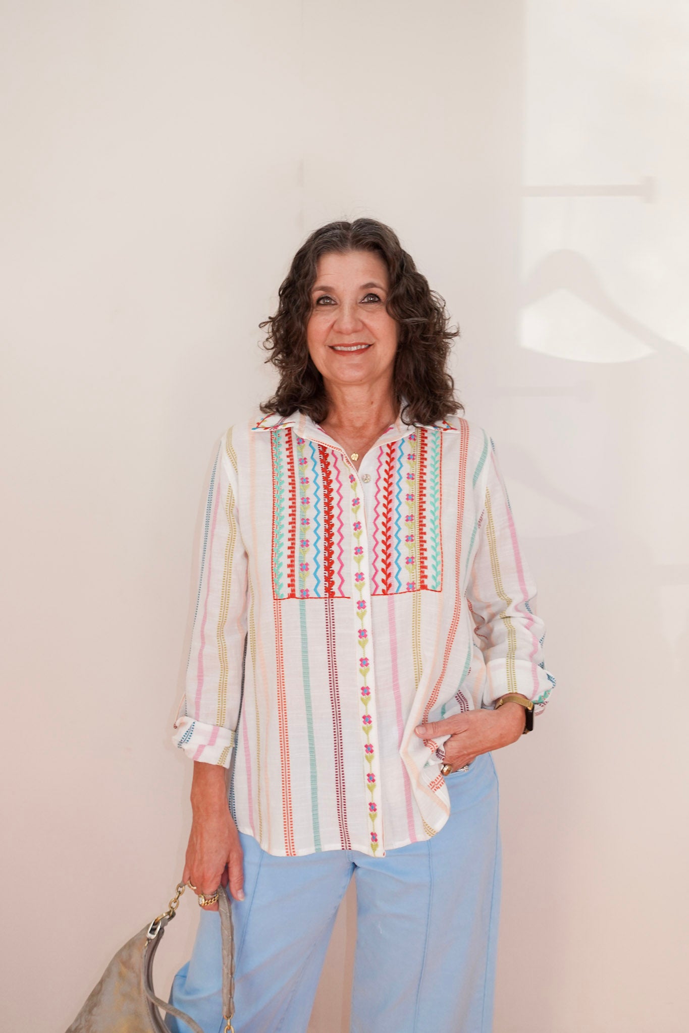 Woman wearing a colorful striped shirt with a geometric pattern on a plain background