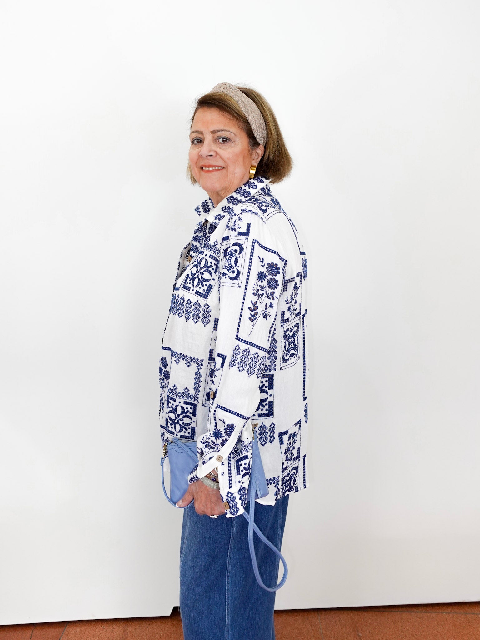 Woman wearing a white blouse with blue patterns and blue jeans against a white background