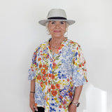 Woman wearing a colorful floral shirt and a hat on a white background