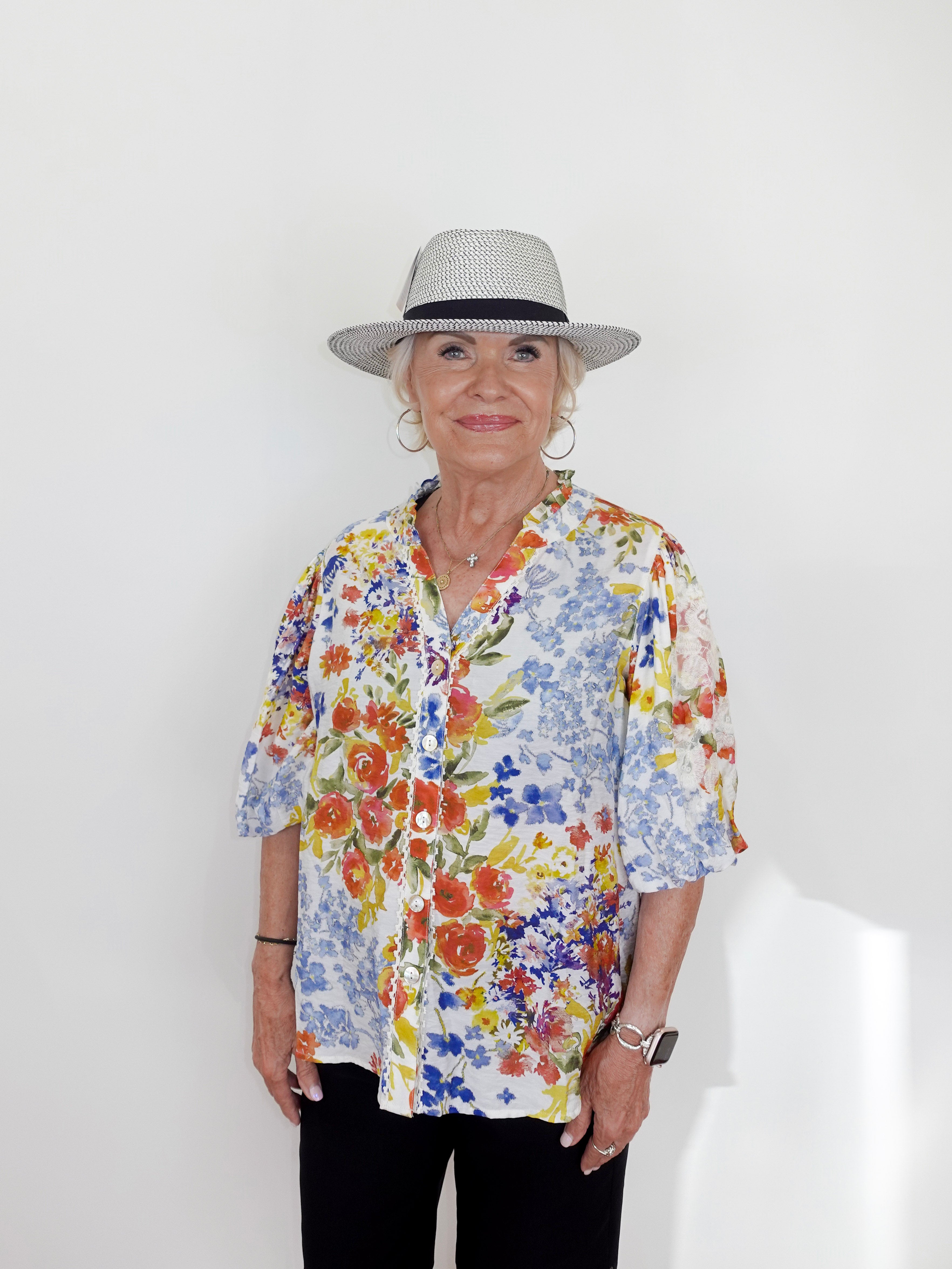 Woman wearing a colorful floral shirt and a hat on a white background
