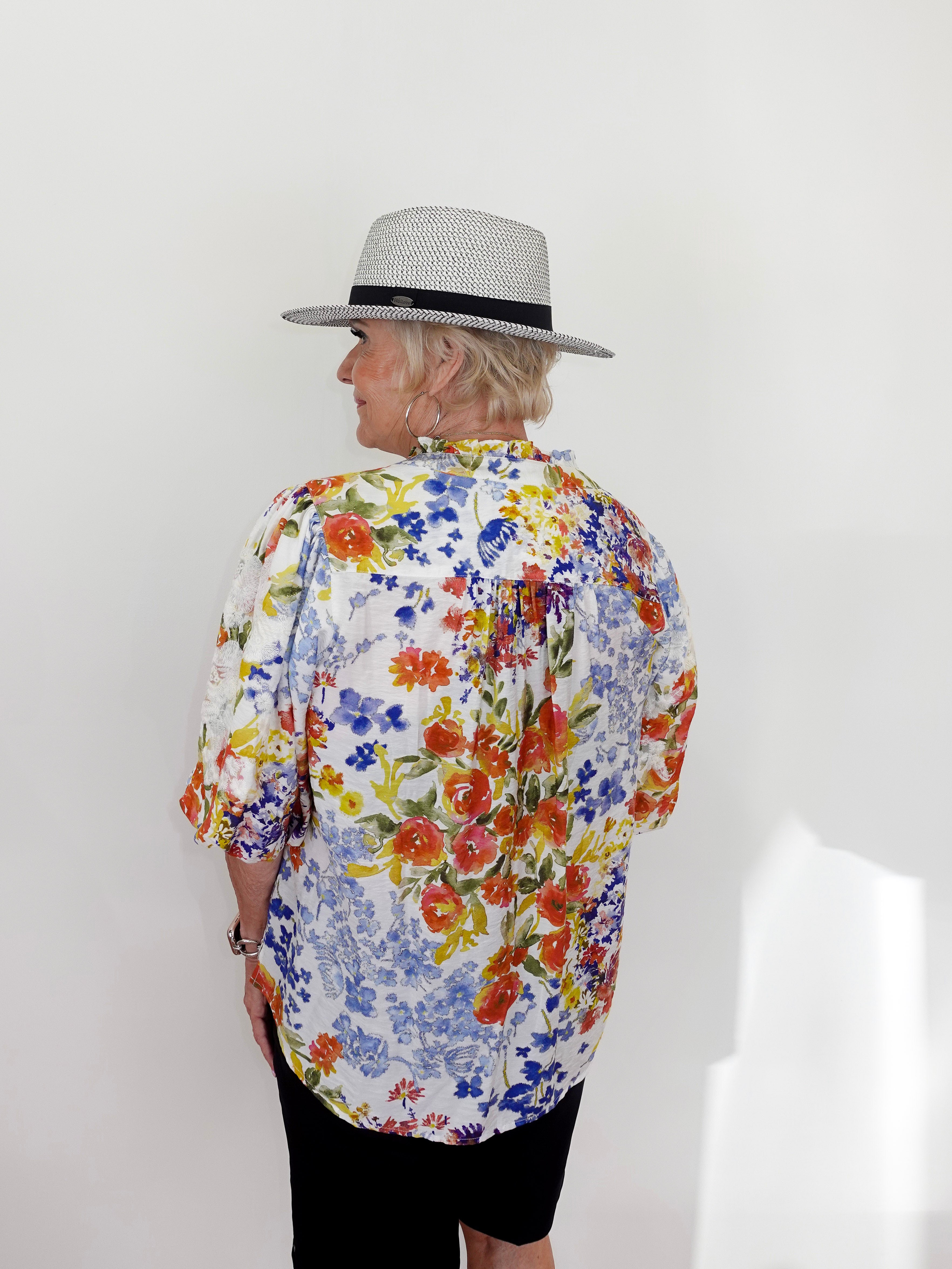 Person wearing a colorful floral shirt and a hat against a white background