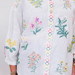 White blouse with colorful floral embroidery on a plain background