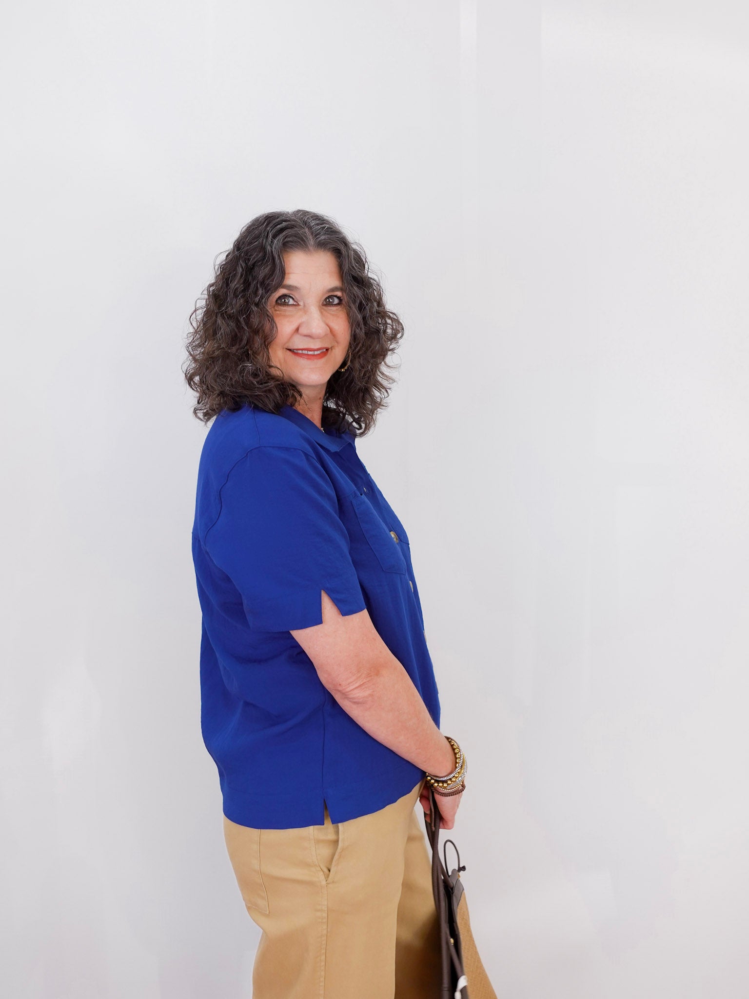 Woman wearing a blue shirt and beige pants against a white background