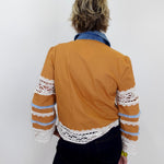 Person wearing a mustard yellow jacket with lace sleeves against a white background